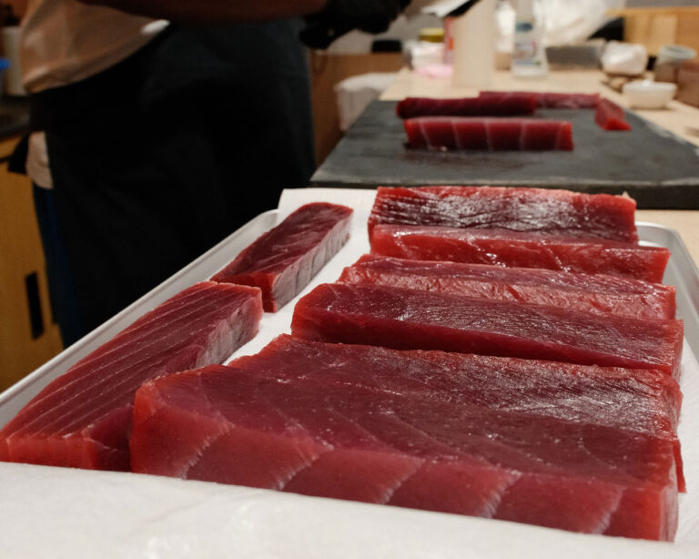 Thick slices of tuna precisely cut and arranged on a wooden board, highlighting knife skills and freshness.