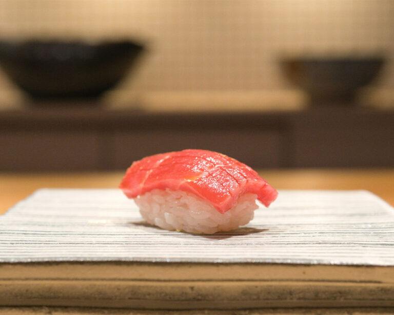 Close-up of Edomae-style tuna sushi with glossy surface and compact rice form, showing precise knife work and traditional technique that preserves freshness and balance of taste.