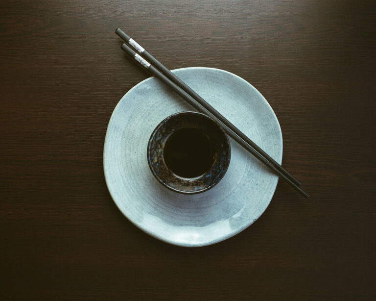 A small ceramic dish filled with dark, glossy soy sauce, its smooth surface reflecting light, representing a simple yet essential condiment used to enhance the flavour of sushi and sashimi.