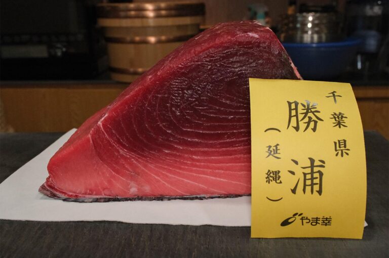 A large, triangular cut of deep red Bluefin Tuna (Akami) from Chiba, Japan, displayed with a yellow label from the famous Yamasachi wholesaler.