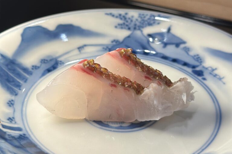Two slices of Madai (red snapper) sashimi with the skin lightly seared, served on a traditional blue and white Japanese porcelain plate.