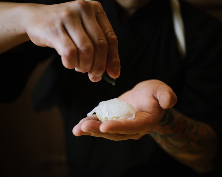 A chef’s hand gently squeezes lime over sushi, adding a fresh citrus aroma and subtle shine.