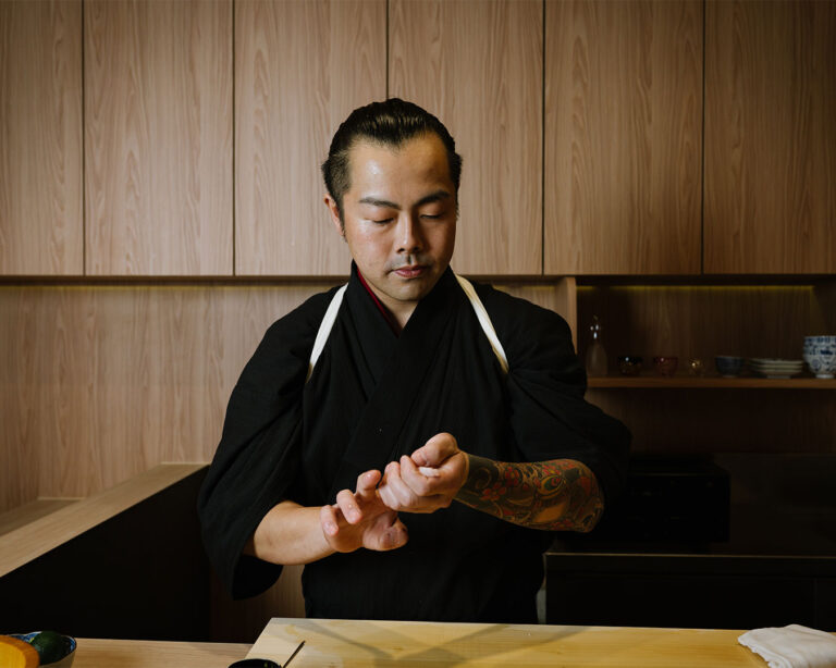 Chef Masa focuses intently while shaping sushi behind the counter, capturing the quiet rhythm and artistry of an authentic omakase experience.