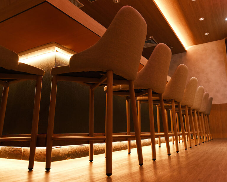 An intimate eight-seat omakase counter with warm lighting and a clean, modern Japanese interior, creating a private dining atmosphere for a personalised sushi experience.