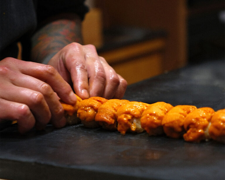A chef’s hand delicately placing sea urchin roe onto sushi rice, demonstrating precision, care, and traditional sushi craftsmanship.