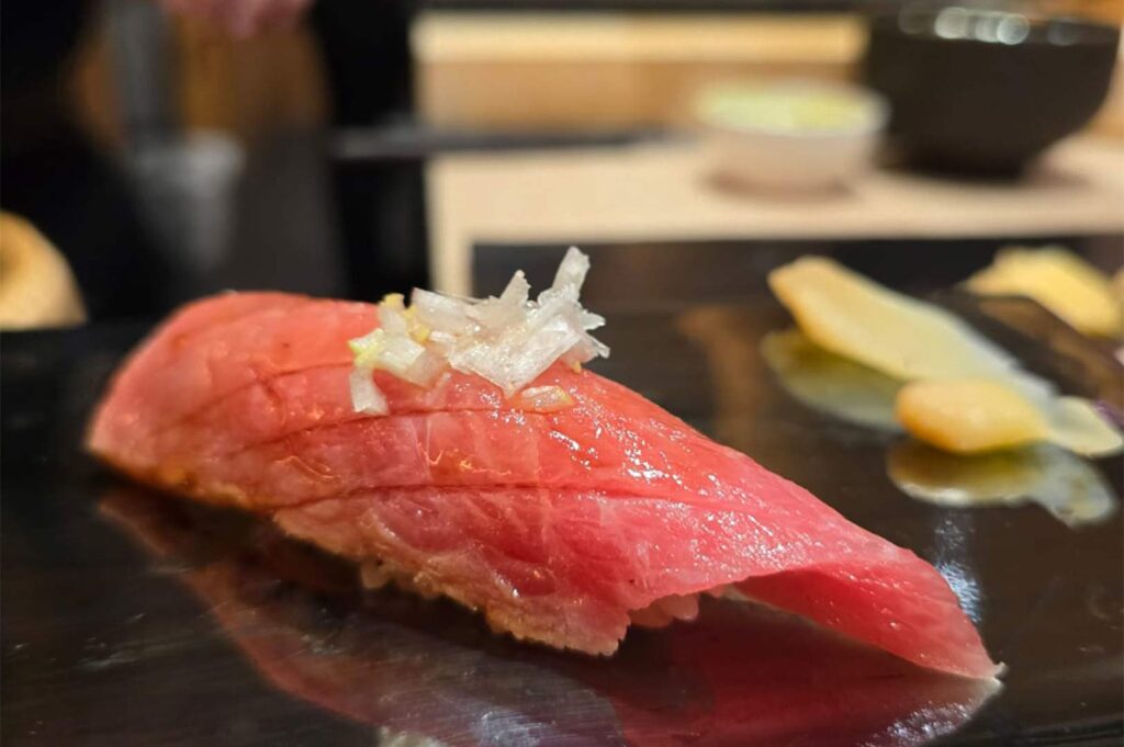 A close-up of a premium bluefin tuna otoro sushi topped with finely chopped white scallions on a black lacquer plate.