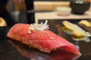 A close-up of a premium bluefin tuna otoro sushi topped with finely chopped white scallions on a black lacquer plate.