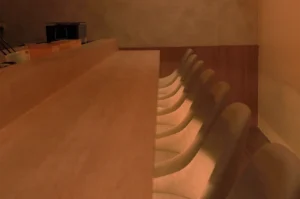 An empty, elegant wooden sushi counter with minimalist beige chairs in a dimly lit, high-end Japanese restaurant.