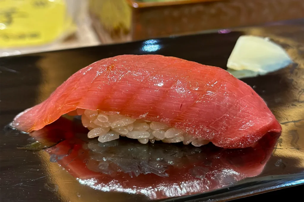 A close-up of a premium tuna (maguro) nigiri sushi served on a black lacquer plate at an omakase restaurant.