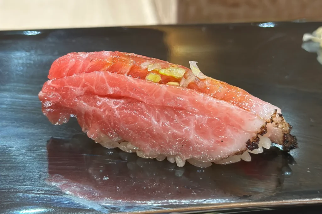 Close-up of a premium seared fatty tuna (Otoro) nigiri sushi with green onion garnish on a black ceramic plate.