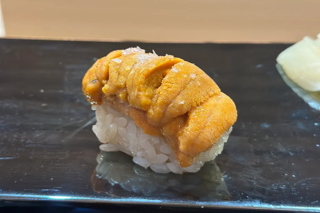High-quality Hokkaido sea urchin (uni) nigiri sushi topped with a pinch of sea salt on a black plate.