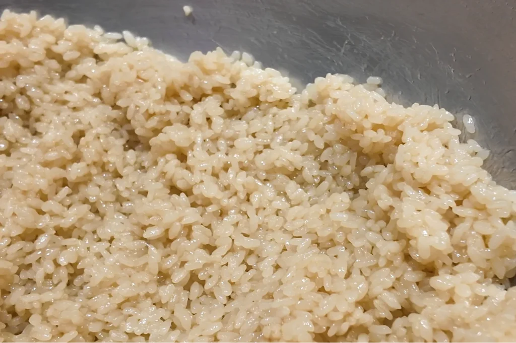 A close-up view of seasoned sushi rice (shari) prepared with traditional red vinegar (akazu), showing individual glossy grains.