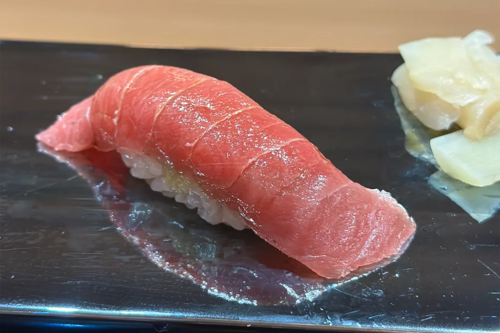 Close-up of a single piece of Chutoro (medium-fatty tuna) nigiri sushi on a black lacquer plate with pickled ginger.
