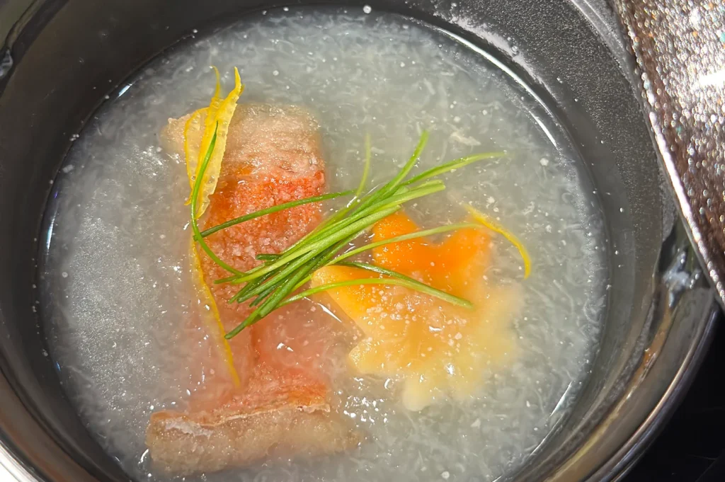 A traditional Japanese clear soup (Suimono) featuring a poached fillet of red-skinned fish, garnishes, and a maple leaf-shaped vegetable.