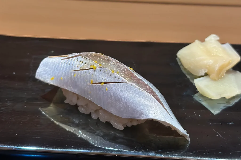 Traditional Kohada (Gizzard Shad) nigiri sushi featuring silver skin with decorative vinegared incisions and citrus zest.