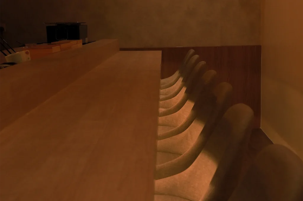 A dimly lit, minimalist luxury sushi bar with warm wooden counters and a row of elegant, modern high-back chairs.