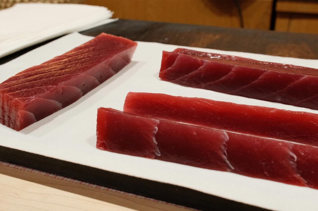 Precision-cut rectangular saku blocks of lean Bluefin Tuna (Akami) arranged on white paper for sushi preparation.