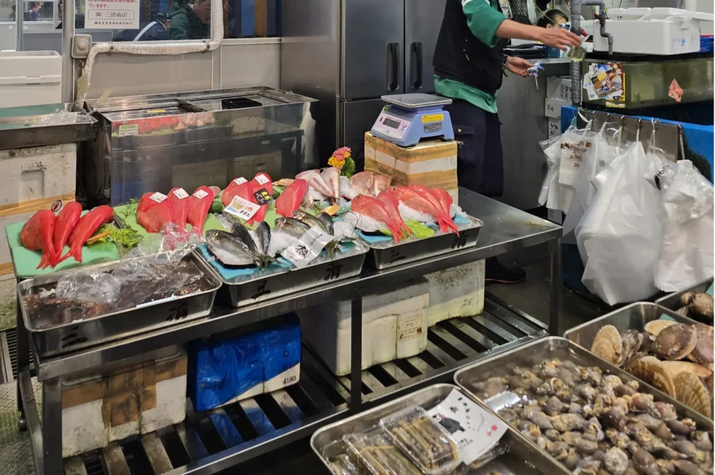 A vibrant display of fresh Kinmedai and other seafood at a Japanese fish market stall, with vendors working in the background.