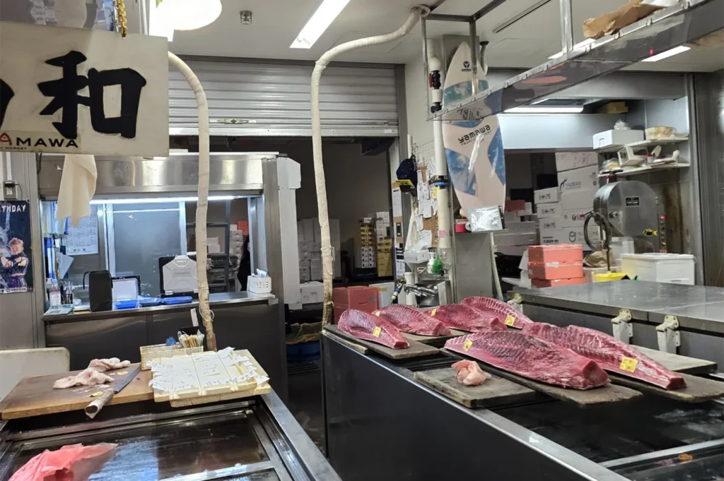 Interior of a Japanese wholesale fish market stall showing large slabs of fresh bluefin tuna on display boards.