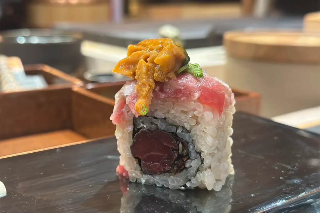 An exquisite sushi roll filled with bluefin tuna, topped with fatty tuna (toro), fresh sea urchin (uni), and green onions.