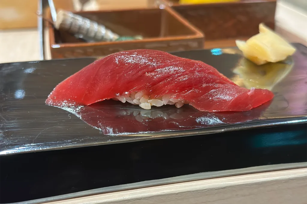 A chef in black gloves precisely portioning a large loin of fresh bluefin tuna on a professional preparation station.
