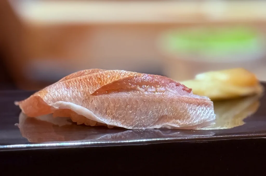 An extreme close-up of a single piece of premium fatty tuna (Otoro) nigiri sushi resting on a glossy black lacquer surface.