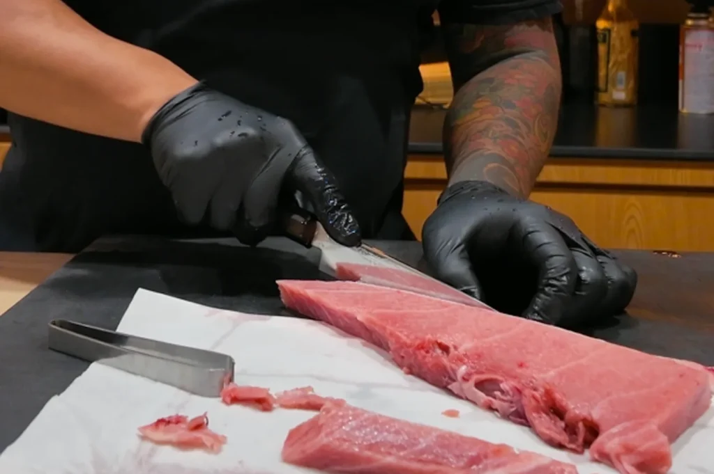 A chef in black gloves precisely portioning a large loin of fresh bluefin tuna on a professional preparation station.