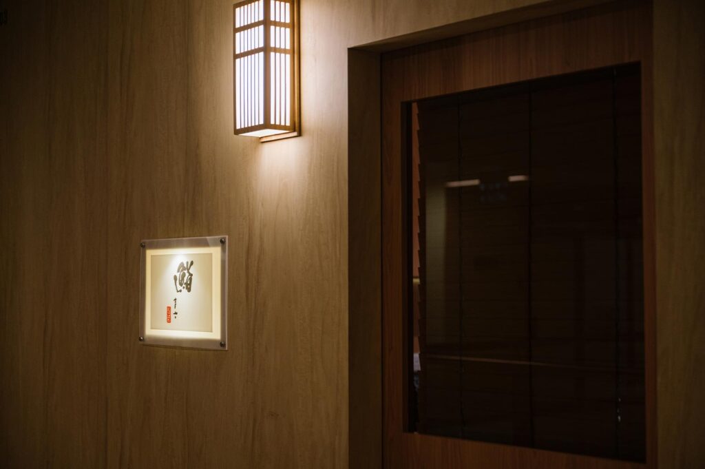 Minimalist exterior entrance of an upscale Japanese sushi restaurant with warm lighting and a traditional 'Sushi' kanji sign.
