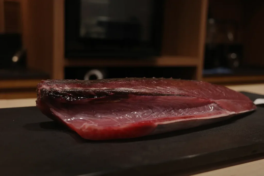 A large, fresh loin of deep red bonito (katsuo) or tuna resting on a black prep board in a professional kitchen.