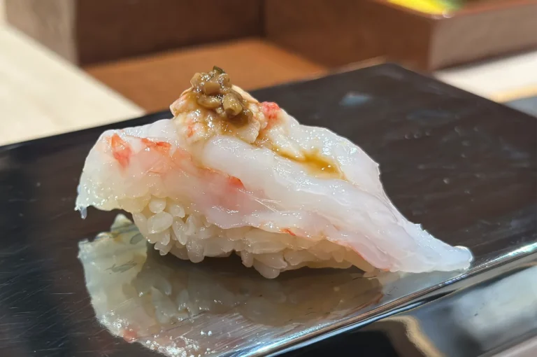 Gourmet sweet shrimp (Amaebi) nigiri sushi topped with savory shrimp miso and a touch of soy sauce on a reflective black plate.