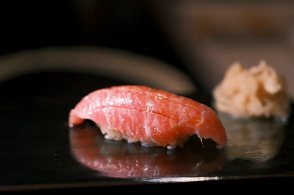 A close-up of a premium fatty tuna (Otoro) nigiri sushi piece served on a black reflective plate with pickled ginger.
