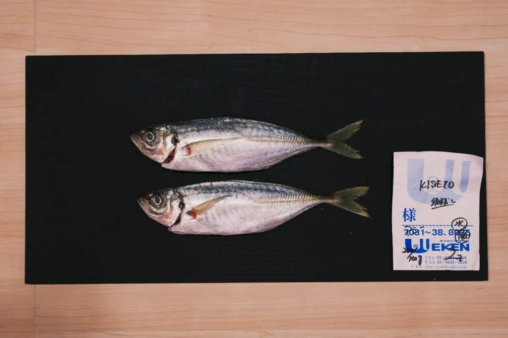 Two fresh fish displayed on a black cutting board with a label to the right, set on a wooden surface. The setting conveys a sense of simplicity.