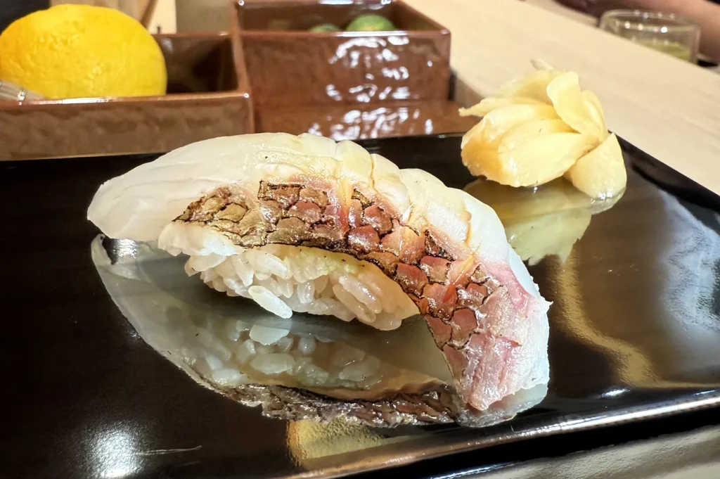 Fresh Madai (Japanese Red Sea Bream) nigiri sushi with skin-on preparation, served on a glossy black lacquer tray with pickled ginger.