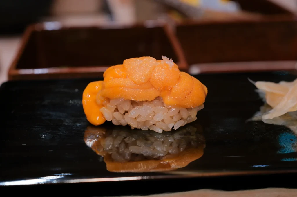 Fresh orange sea urchin (Uni) nigiri sushi with seasoned red vinegar rice (shari) on a black lacquer board.