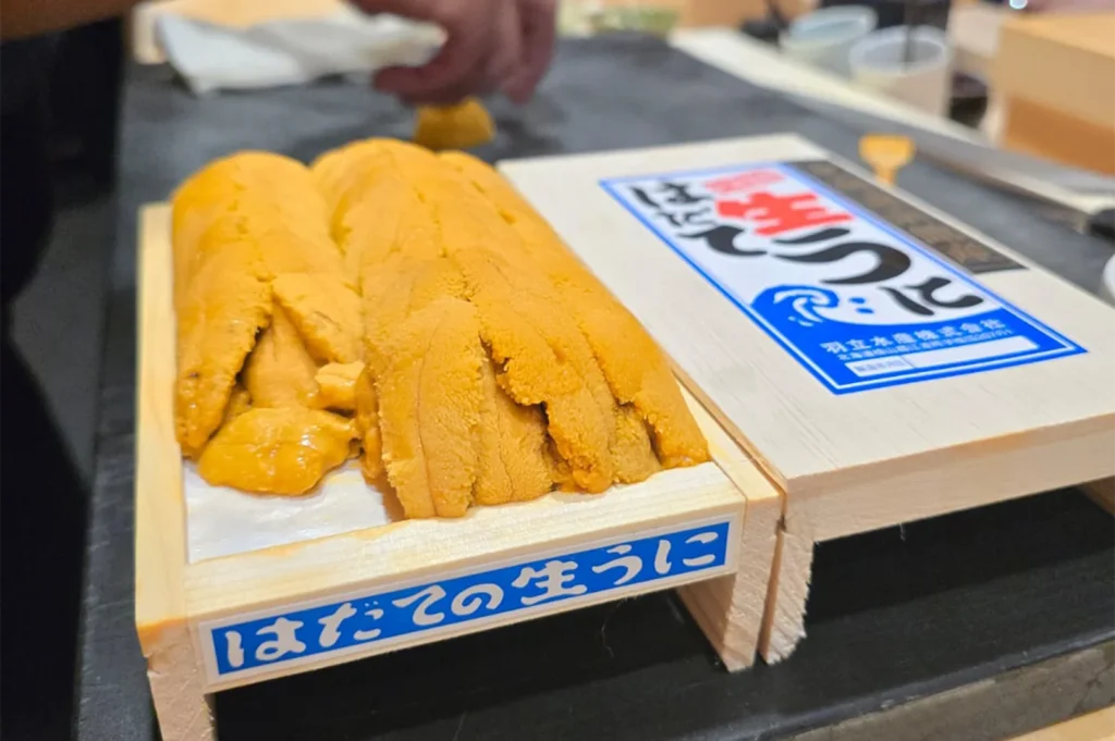 Two wooden trays of high-grade Hadate Nama Uni (fresh sea urchin) from Hokkaido, Japan, showing the vibrant orange color and organized rows of the roe.