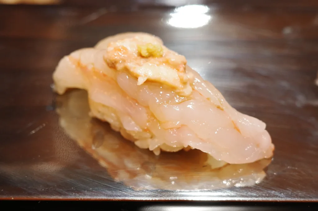 High-end sweet shrimp nigiri sushi featuring a creamy topping and a small dab of fresh green wasabi on a dark wooden surface.