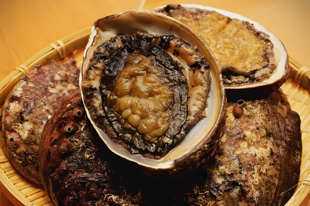 Close-up of a basket with fresh abalones, showcasing their textured, bumpy shells and glossy interiors. The natural tones convey freshness and richness.