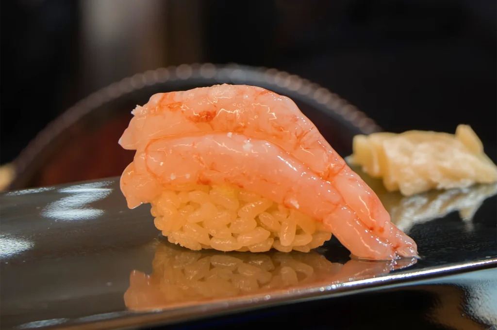 High-quality shrimp nigiri sushi featuring two large, glossy sweet shrimps layered over seasoned vinegar rice on a reflective serving surface.