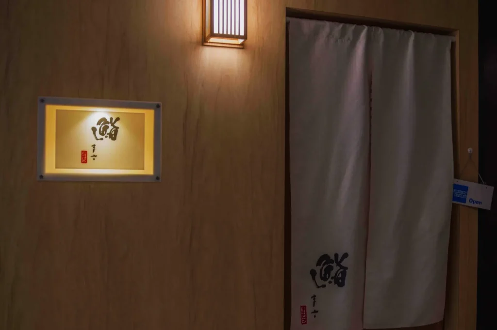 Illuminated wooden wall with a traditional lantern and a draped fabric door. Japanese calligraphy sign adds an elegant, serene ambiance.
