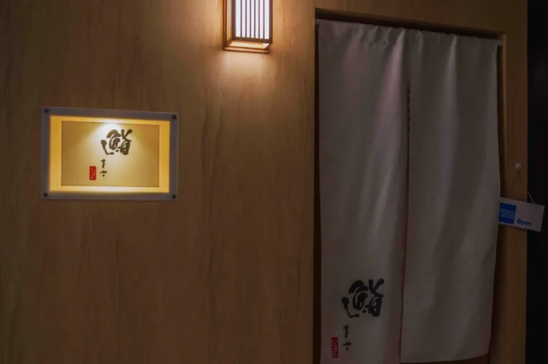 Illuminated wooden wall with a traditional lantern and a draped fabric door. Japanese calligraphy sign adds an elegant, serene ambiance.