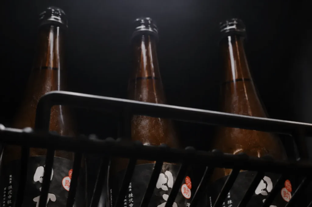 Three brown glass bottles with black and white labels are displayed on a shelf in low lighting, creating a moody and mysterious atmosphere.