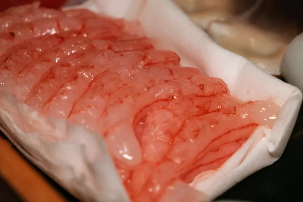 Close-up of raw shrimp with translucent, pink-tinted bodies, neatly arranged on a white cloth. The atmosphere is fresh and appetizing.