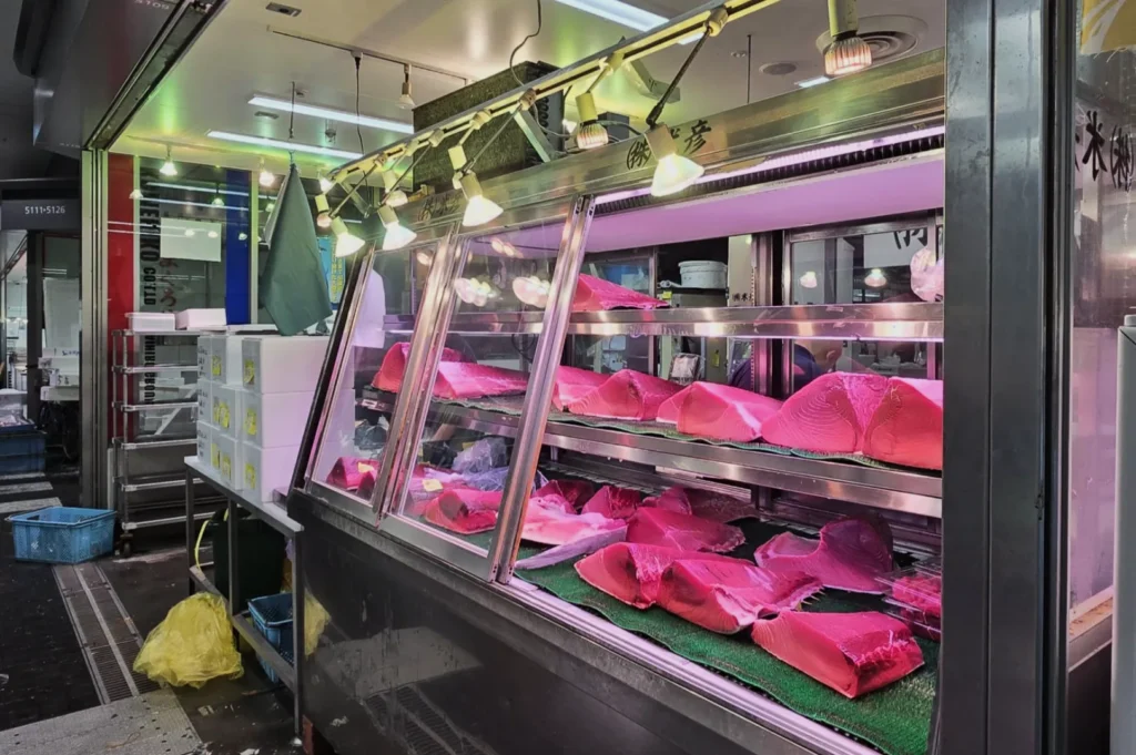 Display case at a fish market showcasing fresh cuts of fish on green trays. Bright overhead lights highlight the vibrant pink hues of the fish.