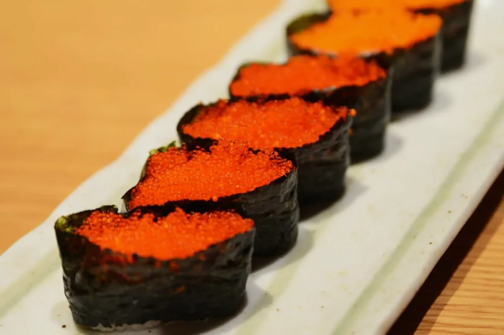 Five pieces of sushi topped with bright orange fish roe, wrapped in seaweed. They are arranged in a row on a rectangular white plate.