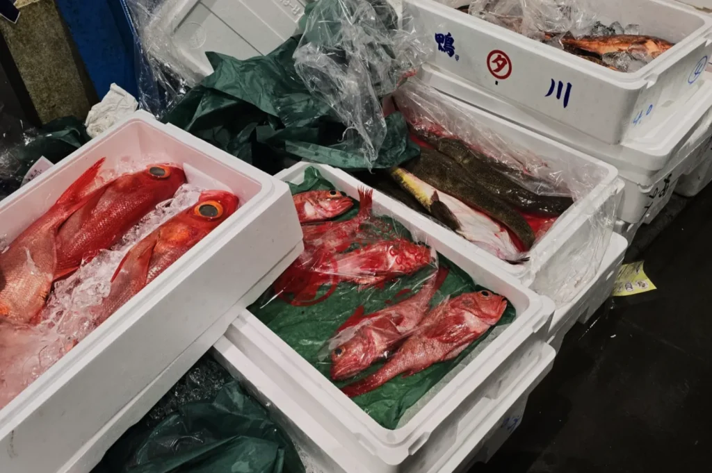 Stacked white foam boxes filled with red fish on ice, surrounded by plastic and green wrapping, create a vibrant, bustling marketplace vibe.