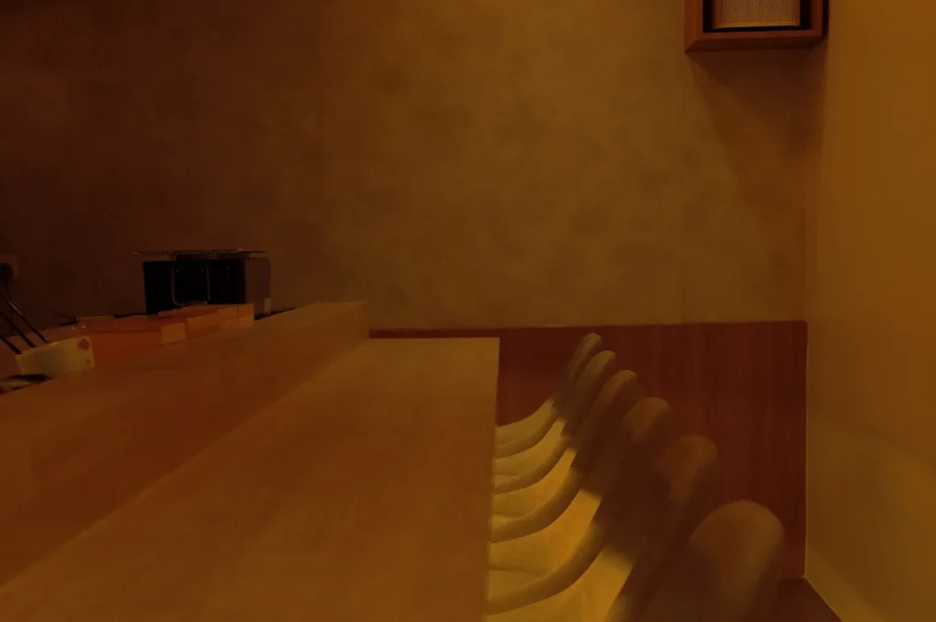 Dimly lit, minimalist space with a wooden bar counter and sleek chairs. Warm tones and shadows create a cozy, intimate ambiance.