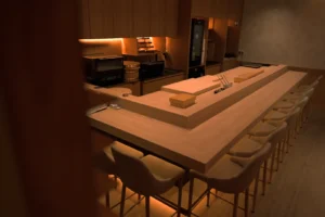 Dimly lit, minimalist sushi bar with wooden interior. A long counter with several chairs surrounds the workspace, conveying a serene, cozy atmosphere.