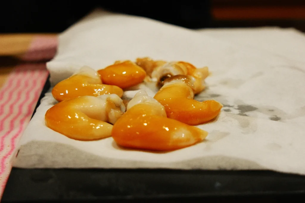 Orange sea snails rest on a paper towel, their glossy shells glistening under soft lighting. The setting is simple with a casual, relaxed feel.