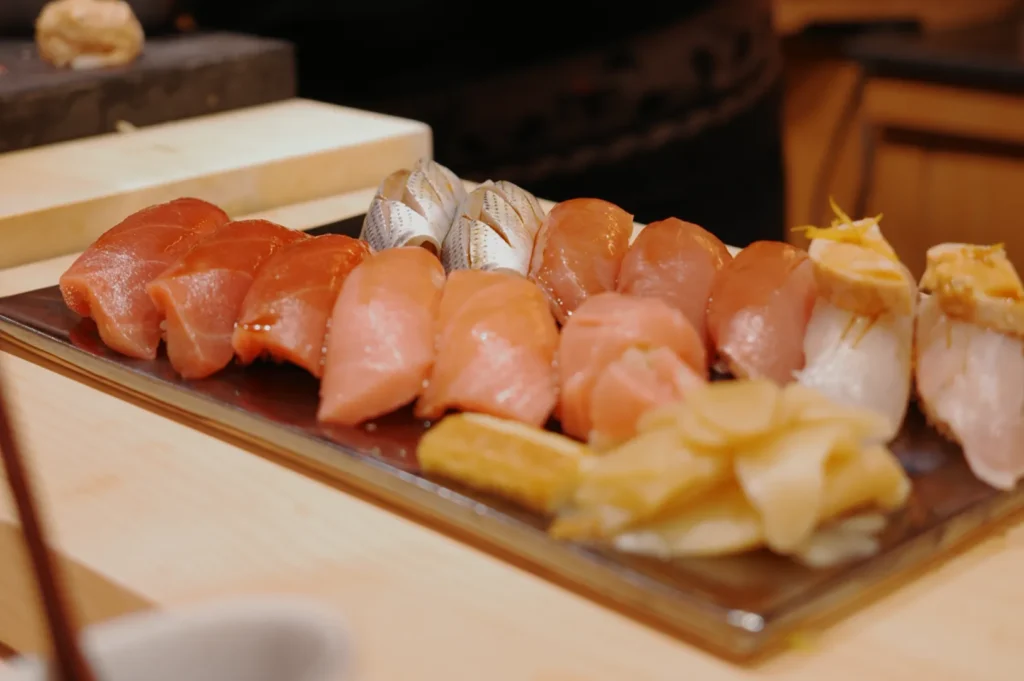 An appetizing platter of assorted sushi, including salmon, tuna, and mackerel, arranged on a wooden surface. The setting is warm and inviting.
