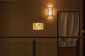 A softly lit wall with a decorative window and a curtain, suggesting an entrance to a room or establishment.